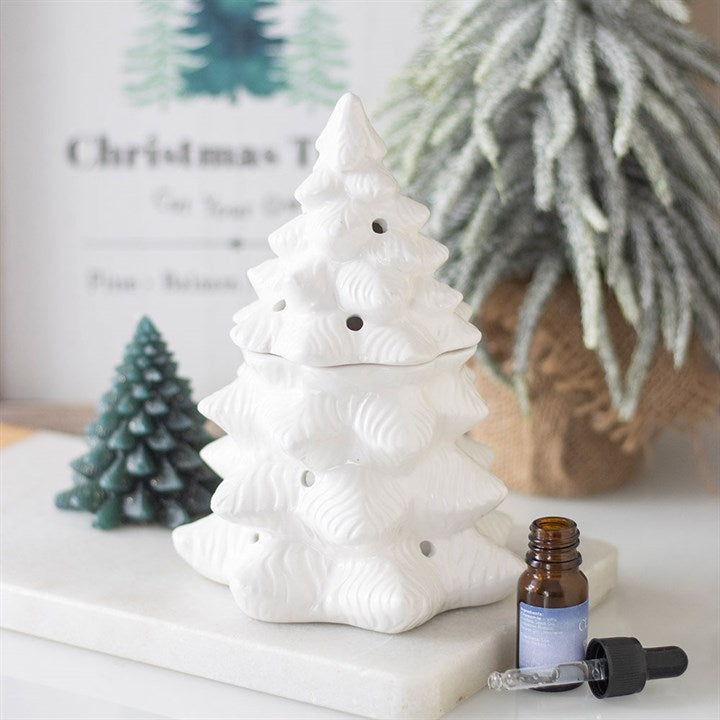 White ceramic Christmas tree with a bottle of essential oil on a white surface.