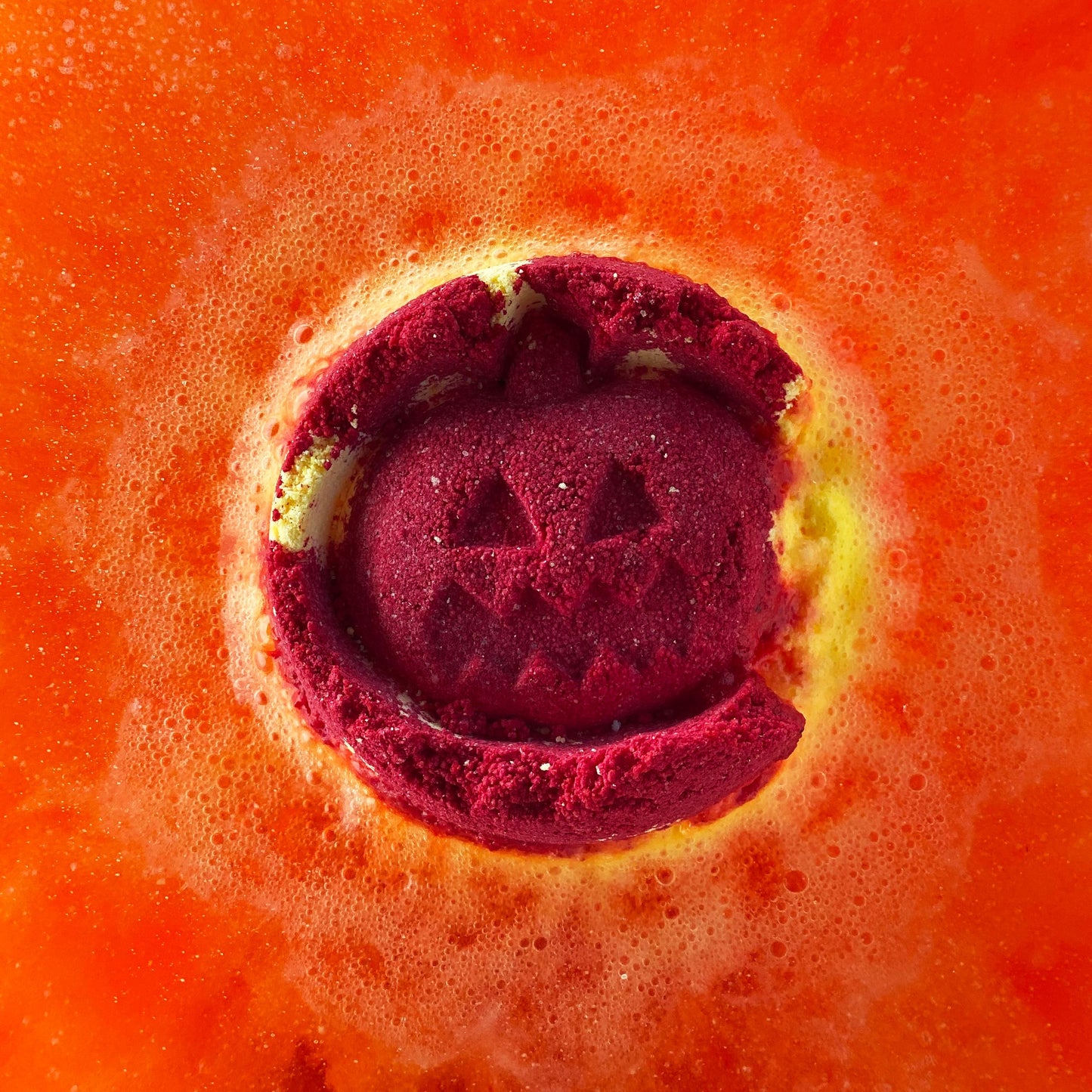 Red bath bomb with a jack-o'-lantern design on an orange background