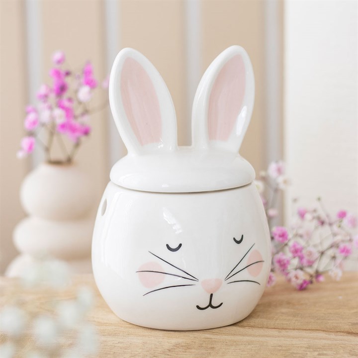 Ceramic bunny jar with a lid on a wooden surface with decorative flowers in the background.