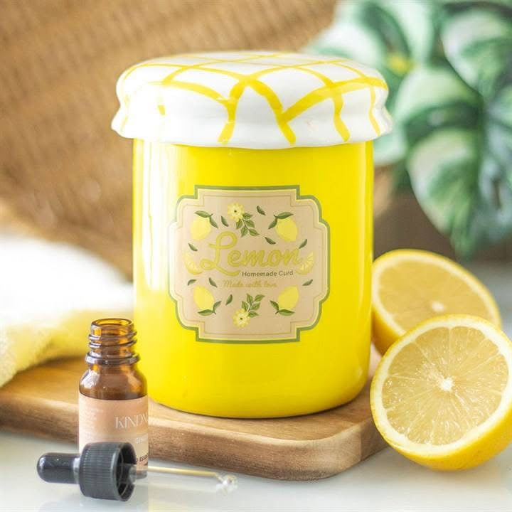 Yellow candle jar labeled 'Lemon' with a bottle of essential oil and lemon slices on a wooden board.