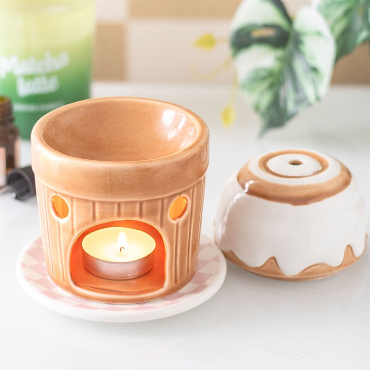 Ceramic candle warmer with a lit candle inside on a white surface.