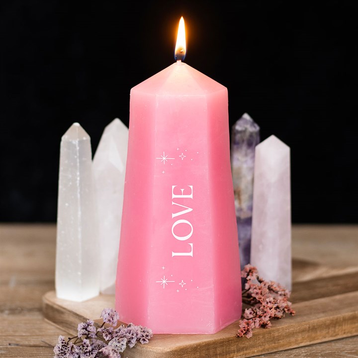 Pink candle with 'LOVE' engraving on a wooden surface with crystals in the background