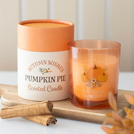 Pumpkin pie scented candle with packaging and cinnamon sticks on a wooden board.
