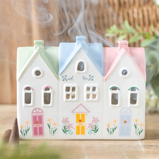Decorative ceramic house-shaped incense burner with pastel colors and floral designs on a wooden surface.