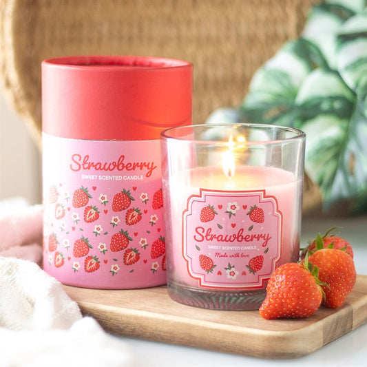 Pink strawberry-scented candle with a red lid on a wooden board, surrounded by strawberries.