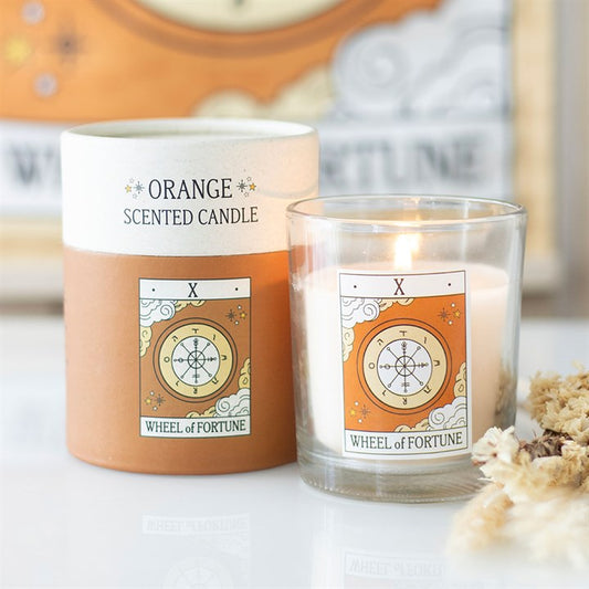 Orange scented candle with 'Wheel of Fortune' label next to its packaging on a light surface.