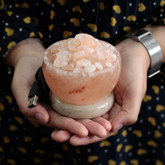 Himalayan salt lamp with USB cable held in hands against a patterned background