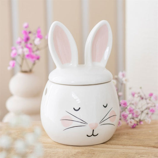 Ceramic bunny jar with a lid on a wooden surface with decorative flowers in the background.