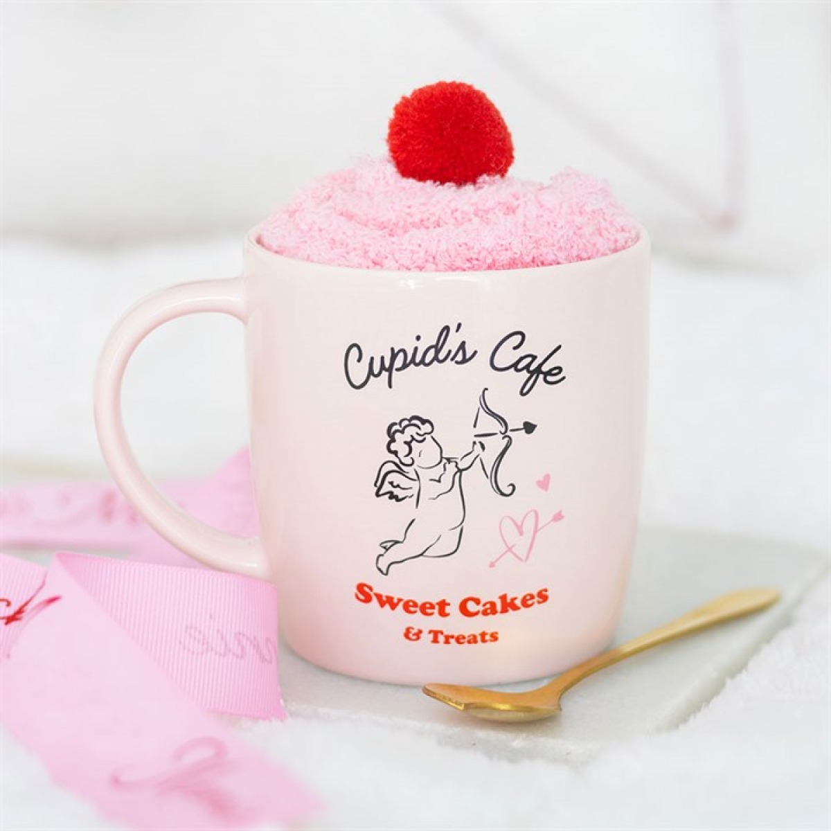 Pink mug with 'Cupid's Cafe Sweet Cakes & Treats' text, topped with pink cake and red cherry, on a white background.