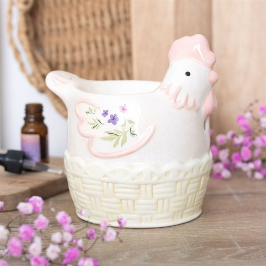 Ceramic chicken-shaped container with floral design on a wooden surface with flowers and a bottle.
