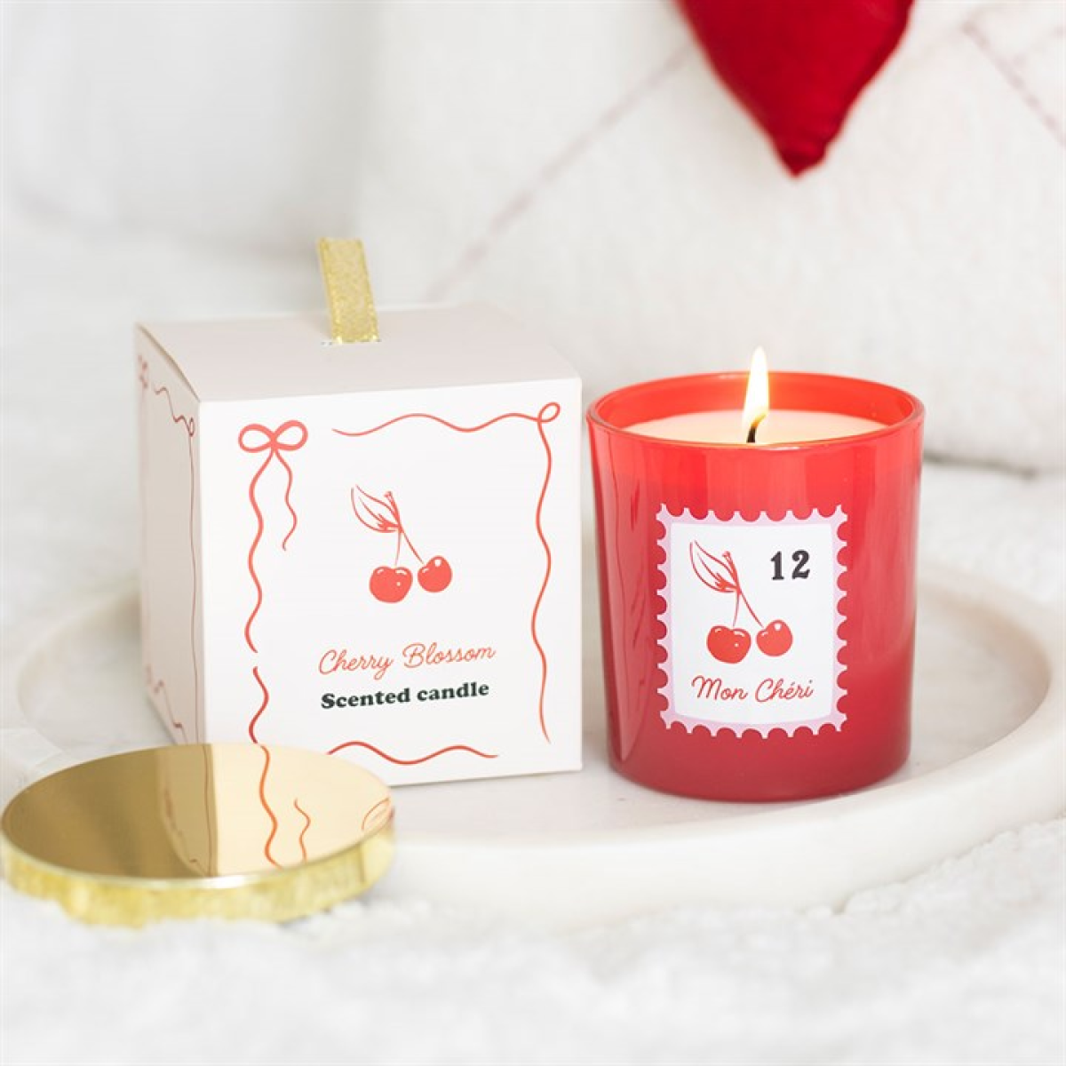 Red scented candle with cherry design and packaging on a white surface