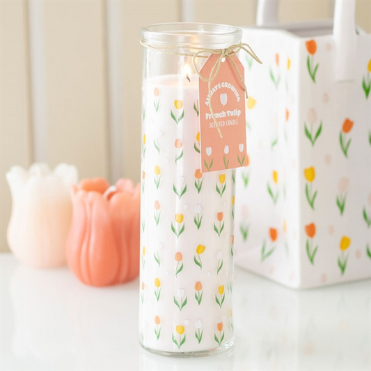 Glass candle with floral design and tag on a white surface