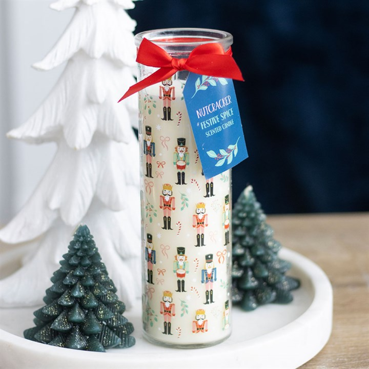 Decorative candle with nutcracker design and red bow, surrounded by small Christmas trees.