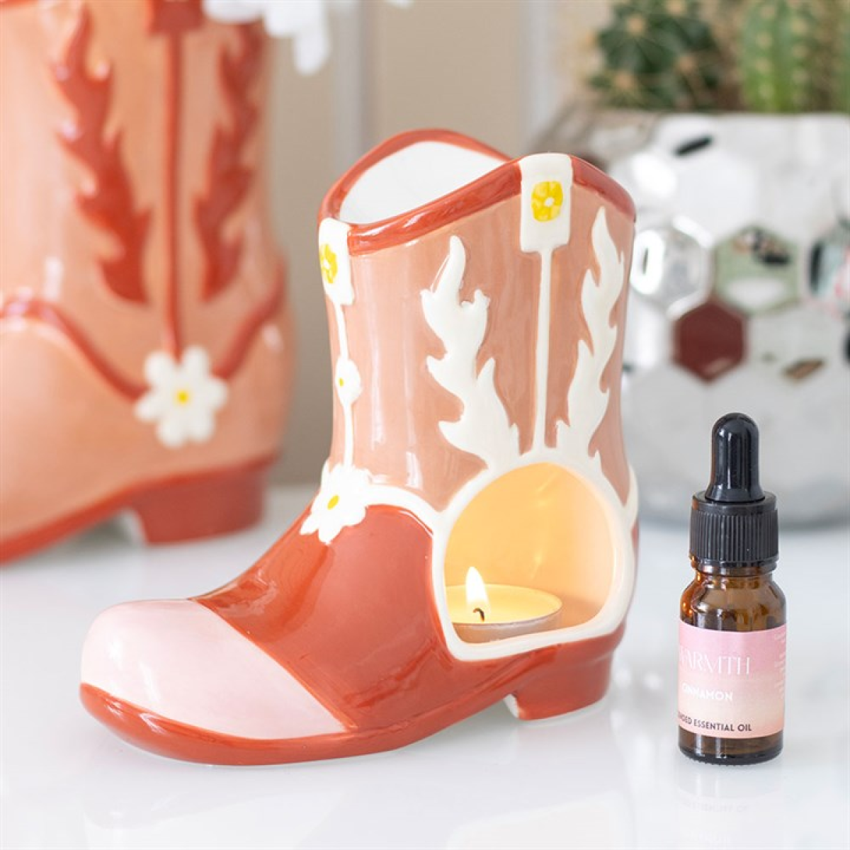 Decorative candle shaped like a boot with flowers and a bottle of essential oil on a white surface.