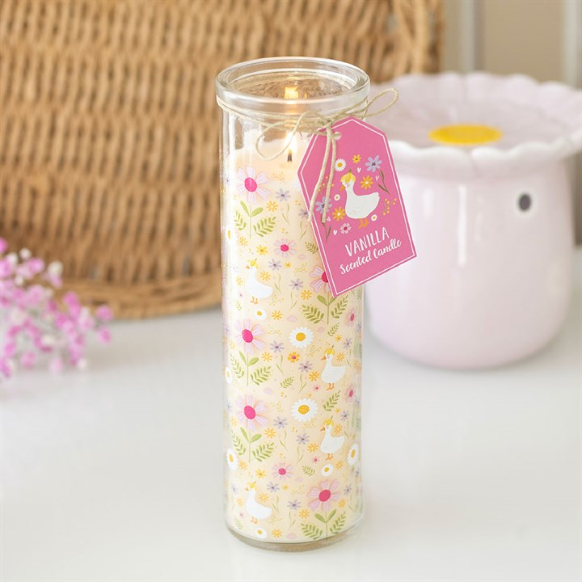 Decorative candle in a glass jar with a floral label on a light surface.