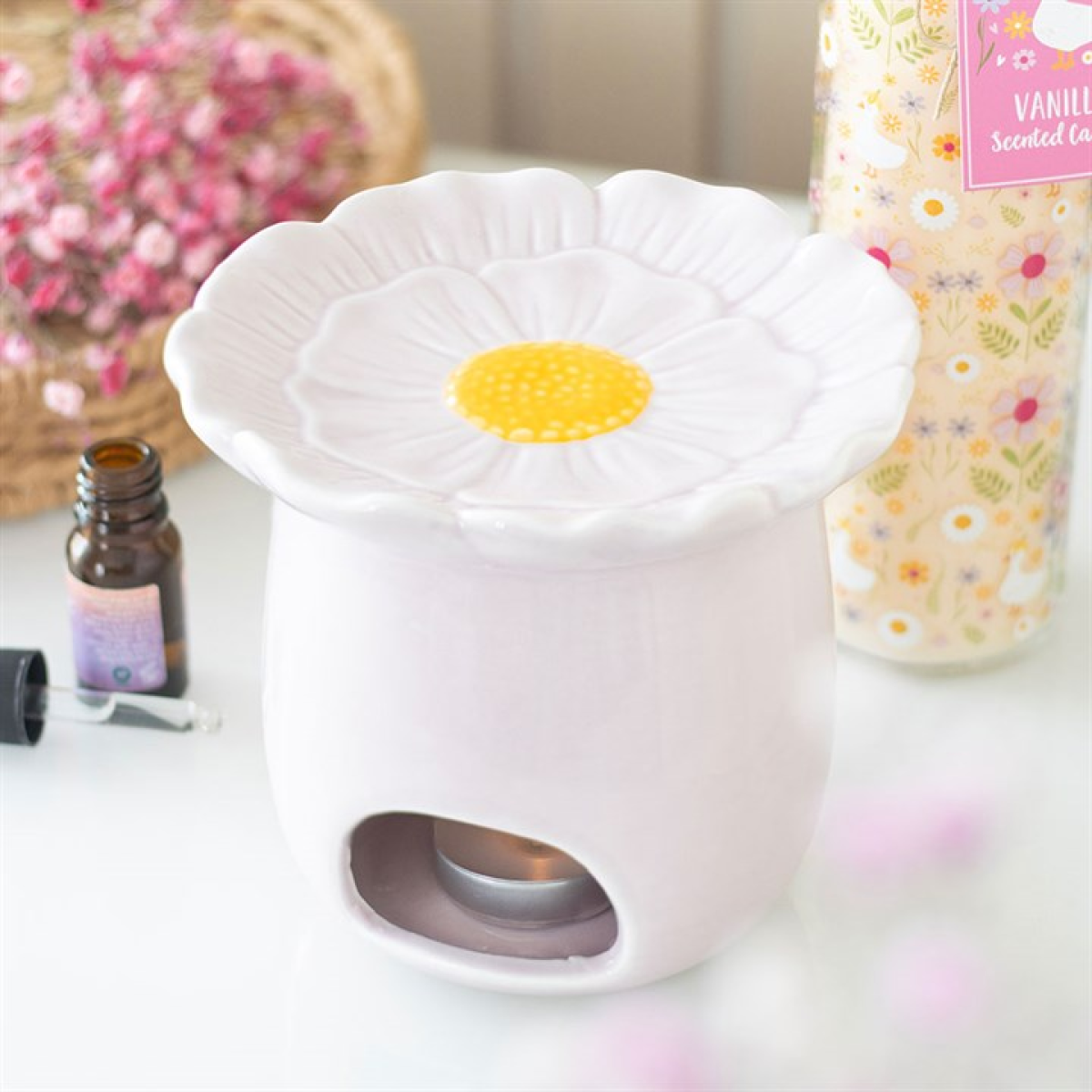White flower-shaped diffuser on a table with essential oil bottle and vanilla scented candle in the background.