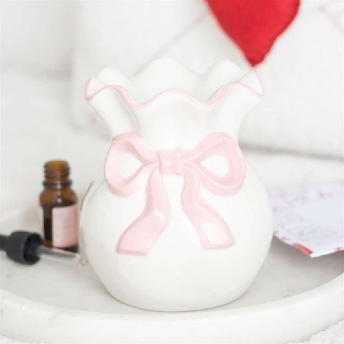 White ceramic jar with a pink bow on a white surface with a blurred background