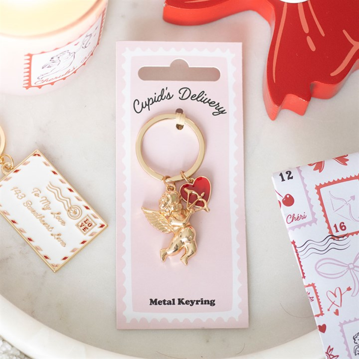Gold cupid keychain on a 'Cupid's Delivery' card with decorative elements.