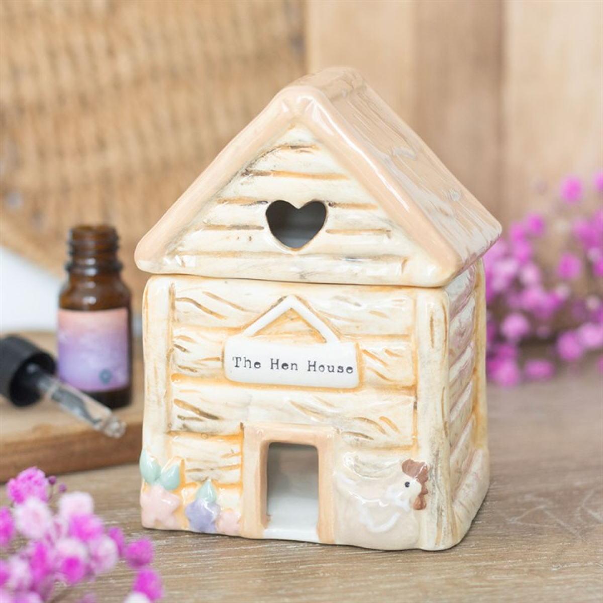 Decorative house-shaped lantern with 'The Hen House' label on a wooden surface with flowers and a bottle.