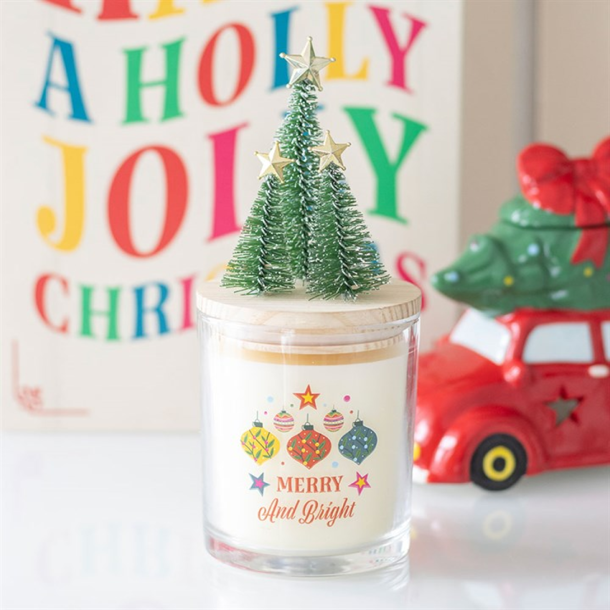 Decorative candle with a small Christmas tree on top, featuring colorful ornaments and 'Merry and Bright' text.