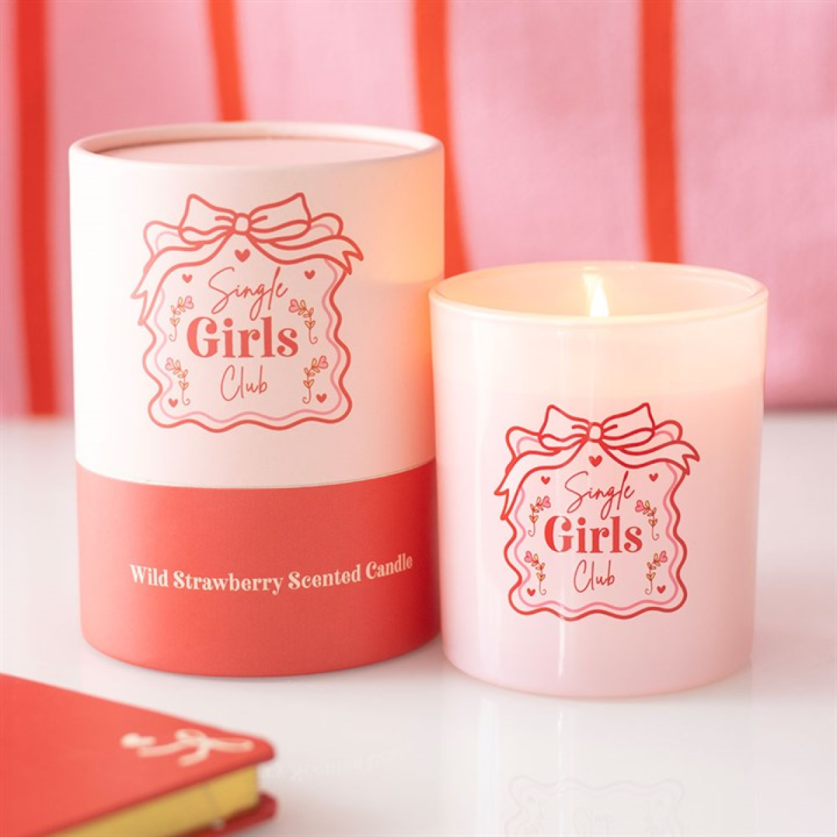 Pink candle with 'Single Girls Club' branding next to its packaging on a pink background