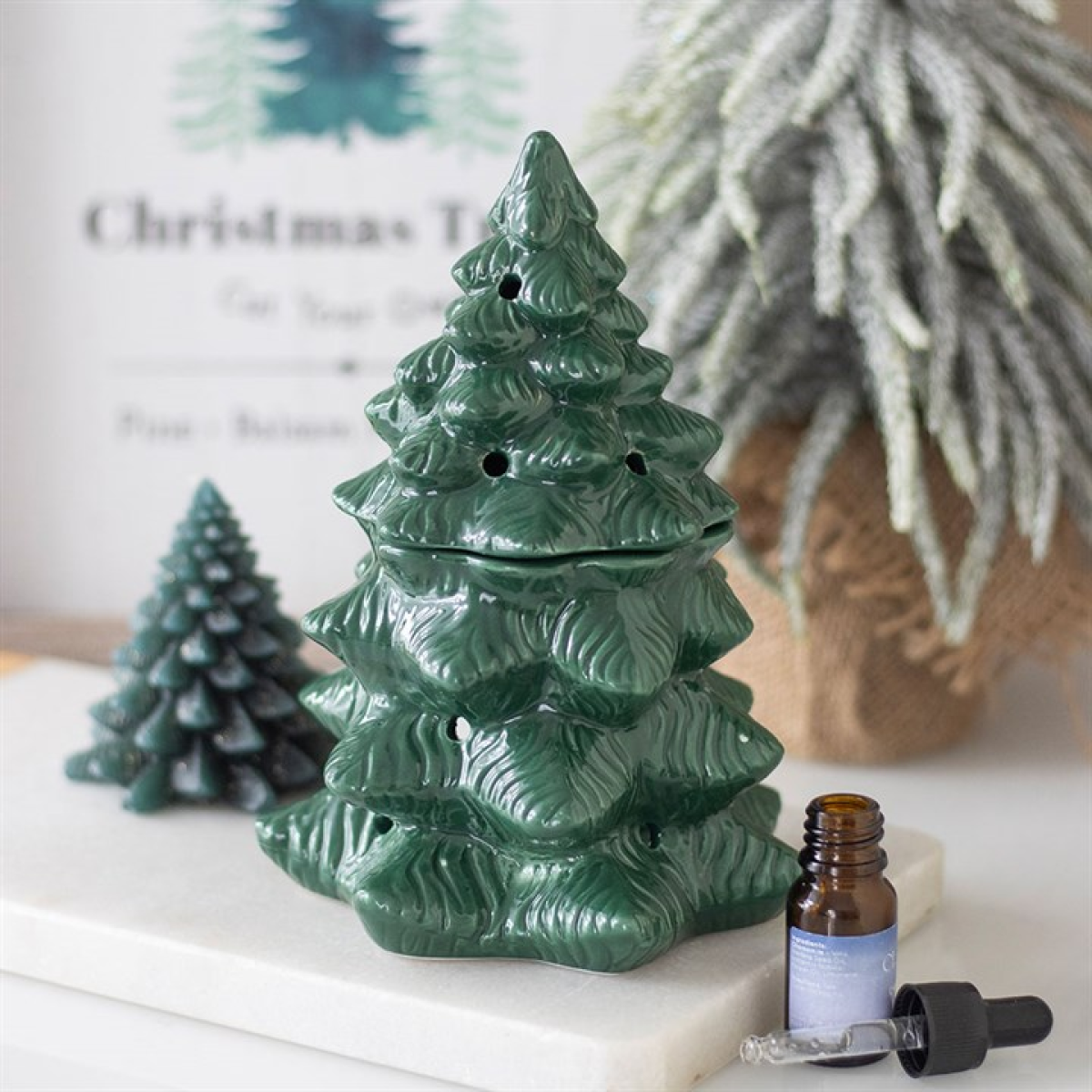 Green ceramic Christmas tree with a small bottle of essential oil on a white surface.