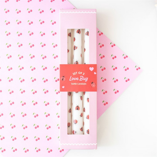 Set of two Love Bug taper candles in a pink box on a pink background with cherry pattern