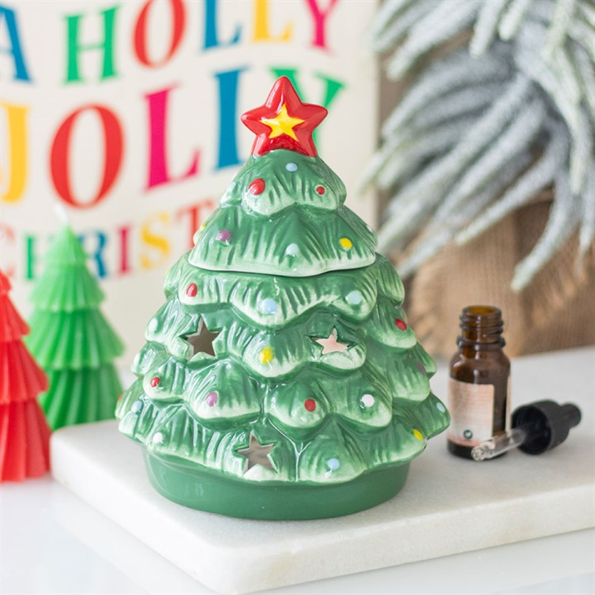 Green Christmas tree-shaped candle with a red star on top, surrounded by colorful letters and a bottle.