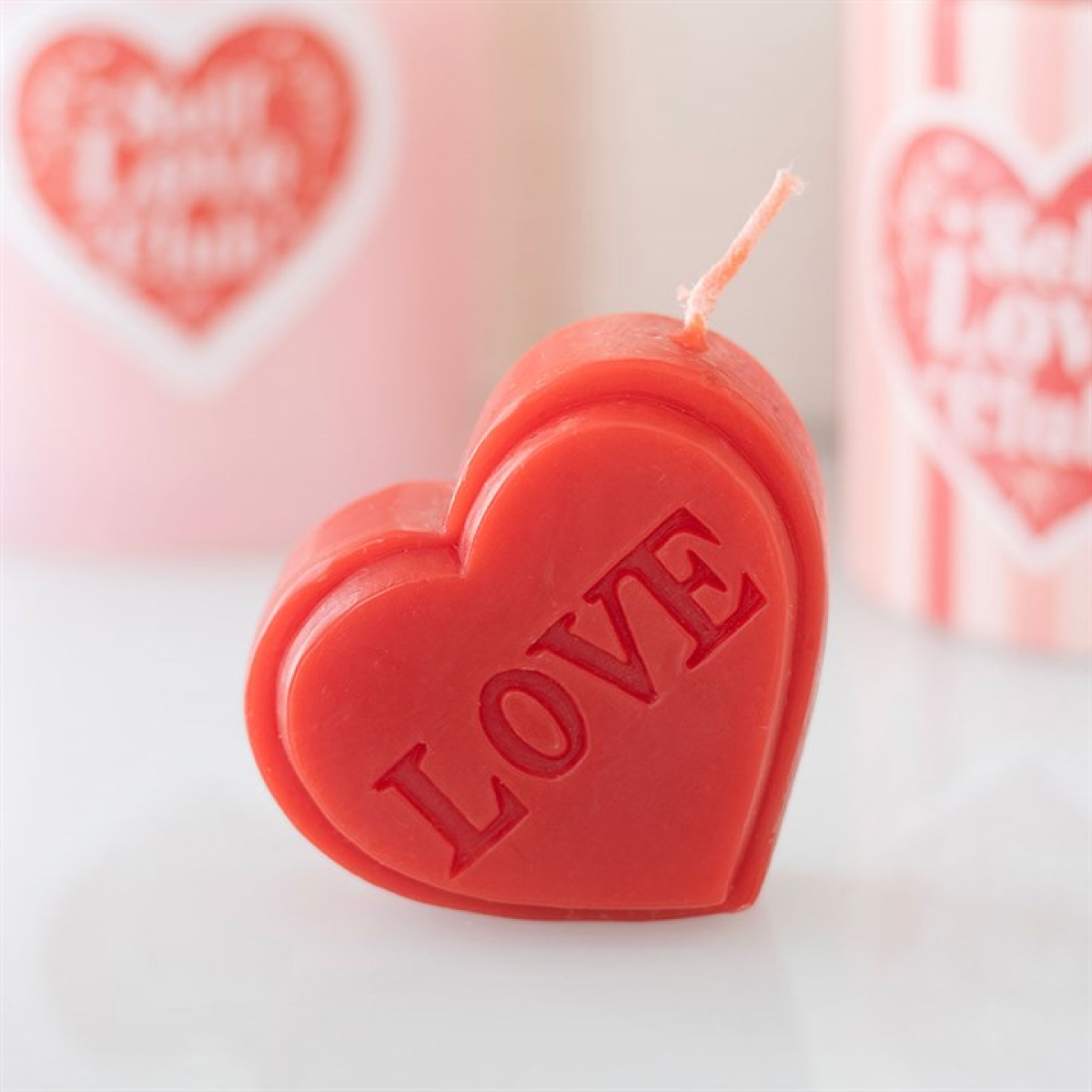 Heart-shaped candle with 'LOVE' embossed on it, set against a blurred background with similar candles.