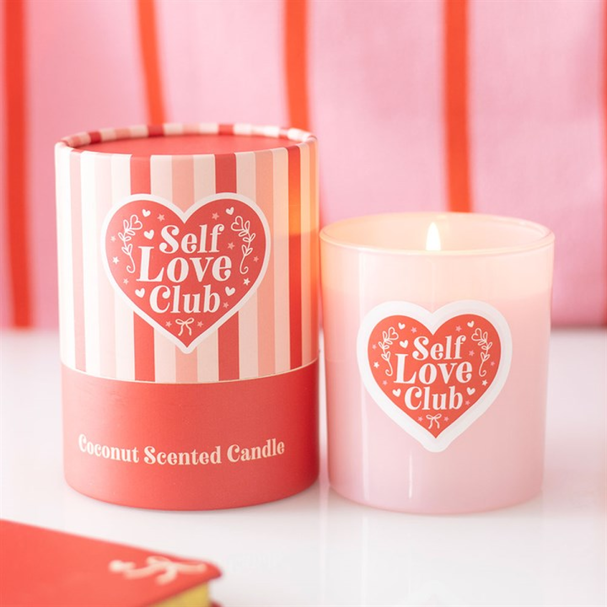 Pink candle with 'Self Love Club' design next to its packaging on a pink background
