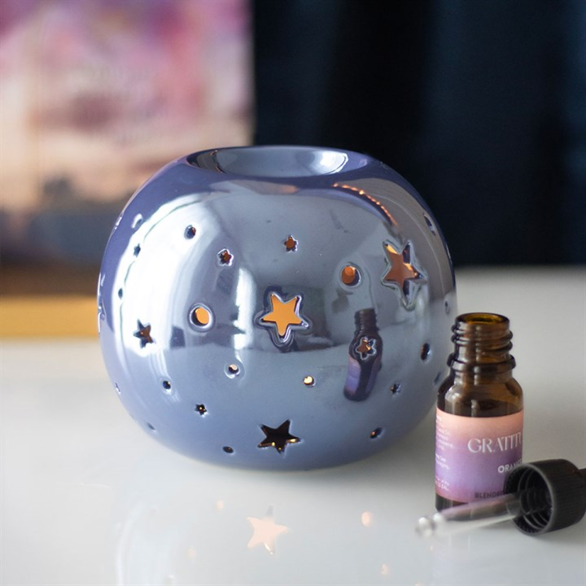 Decorative ceramic holder with star designs and a bottle of essential oil on a light surface.